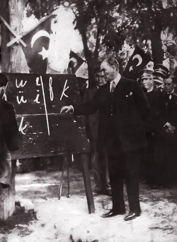 Mustafa Kemal'in açık havada, üzerinde yeni Türk harfleri yazılı kara tahtanın yanında durup halka harfleri anlattığı siyah-beyaz fotoğraf