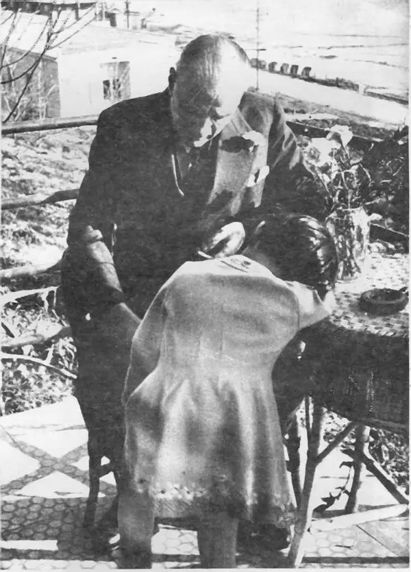 Atatürk'ün bir terasta, hasır masanın yanında oturmuş, önünde duran manevi kızı Ülkü'ye eğildiği siyah-beyaz fotoğraf