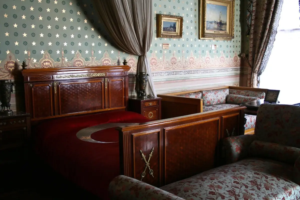 Dolmabahçe Sarayı'nda Atatürk'ün son günlerini geçirdiği oda: ay yıldızlı kırmızı bayrak örtüsüyle kaplı ahşap karyola, çiçek desenli koltuklar, sehpada küçük bir saat ve perdeli pencere
