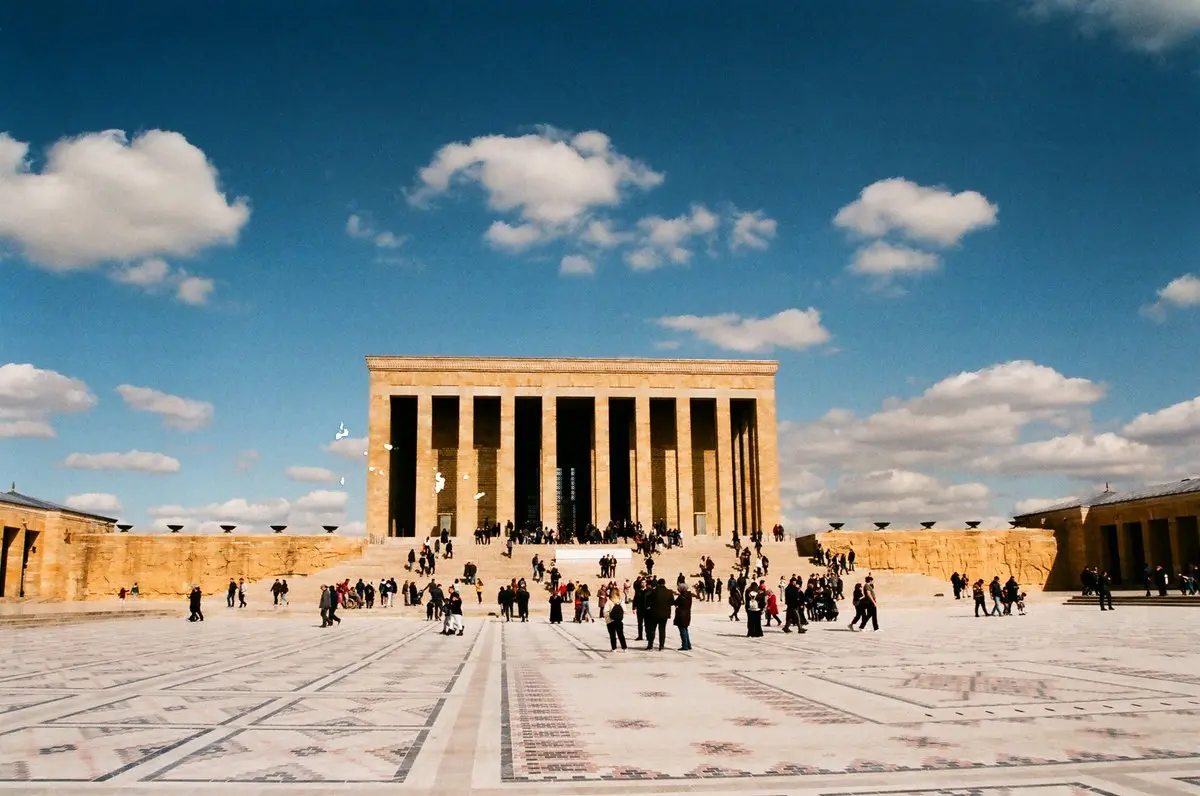 Ankara'da Anıtkabir'in Tören Meydanı ve sütunlu Şeref Holü, açık mavi gökyüzü altında meydanda yürüyen ziyaretçiler