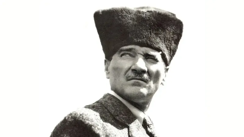 Mustafa Kemal Atatürk'ün kalpaklı, ceketli ve kravatlı hâliyle omuz hizasından çekilmiş siyah-beyaz portresi
