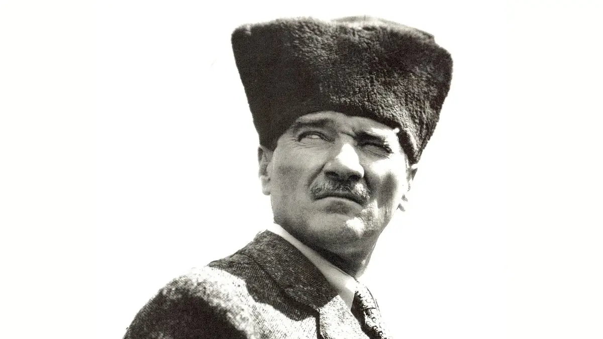 Mustafa Kemal Atatürk'ün kalpaklı, ceketli ve kravatlı hâliyle omuz hizasından çekilmiş siyah-beyaz portresi