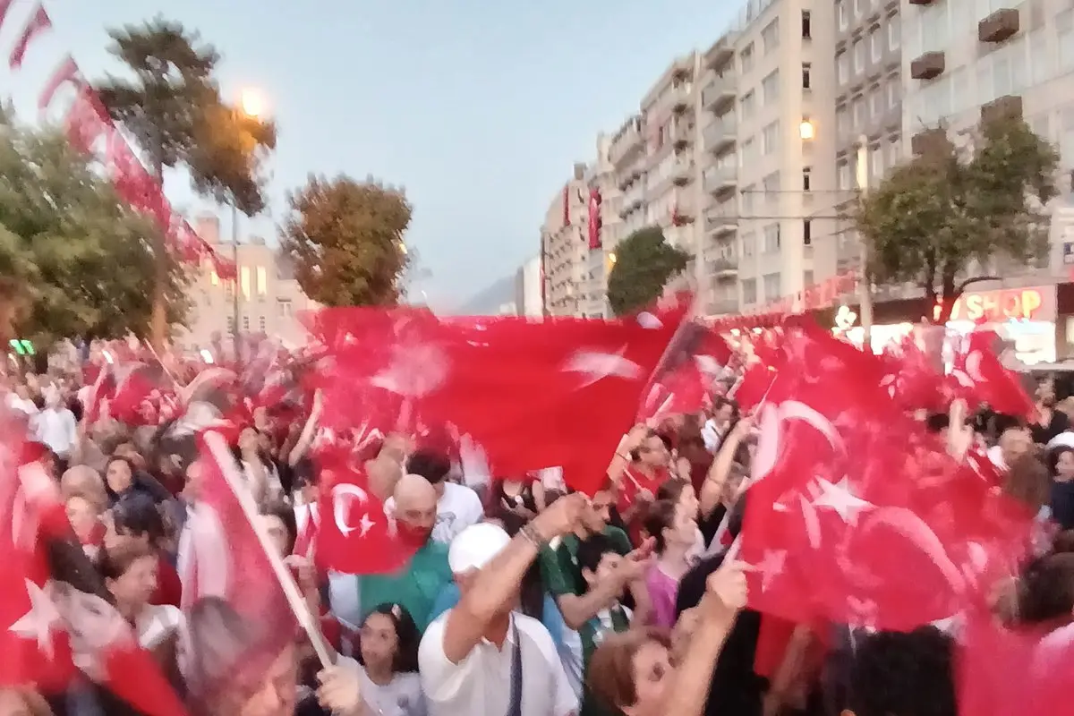 Akşamüstü apartmanlar arasındaki caddede elindeki Türk bayraklarını sallayarak yürüyen kalabalık bir fener alayı