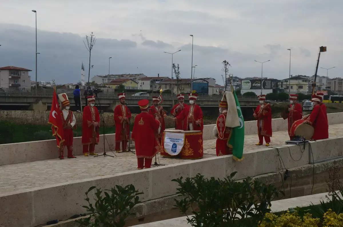 Kırmızı geleneksel kıyafetli mehter takımı açık havada davul, kös ve zurnalarla dizilmiş halde gösteri yapıyor