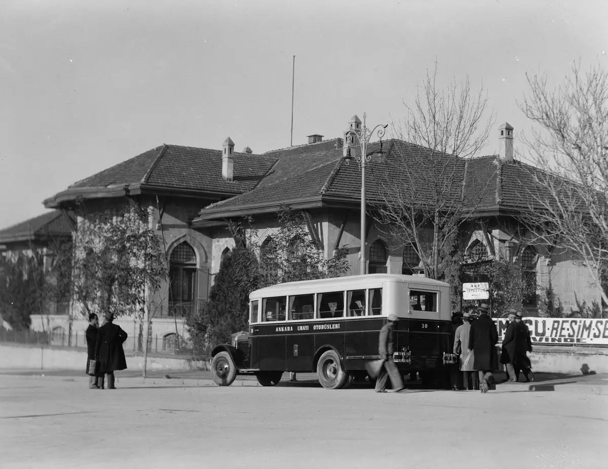 1935'te Ankara'da kiremit çatılı eski Meclis binasının önünde duran Ankara Şehri Otobüsleri yazılı otobüs ve paltolu yolcular, siyah beyaz