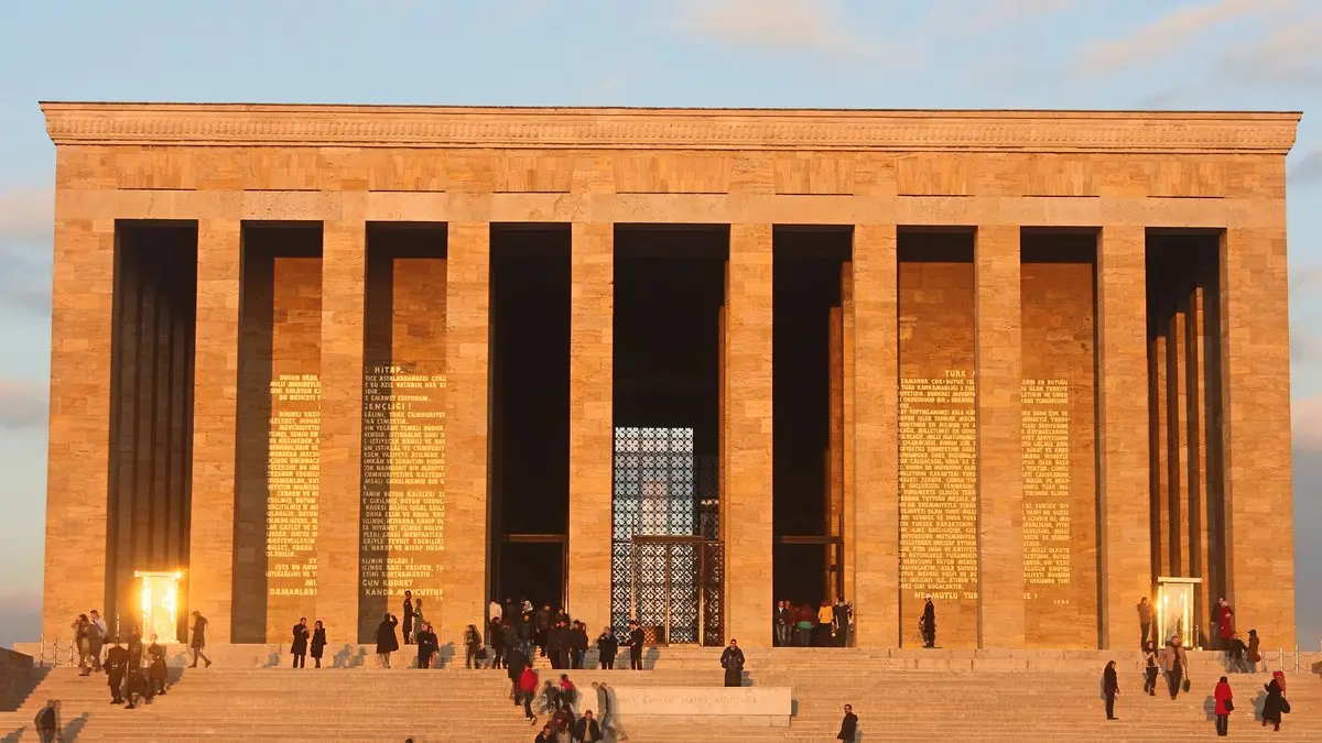 Gün batımında turuncu ışıkla aydınlanan Anıtkabir'in sütunlu Şeref Holü ve önündeki merdivenlerde yürüyen ziyaretçiler