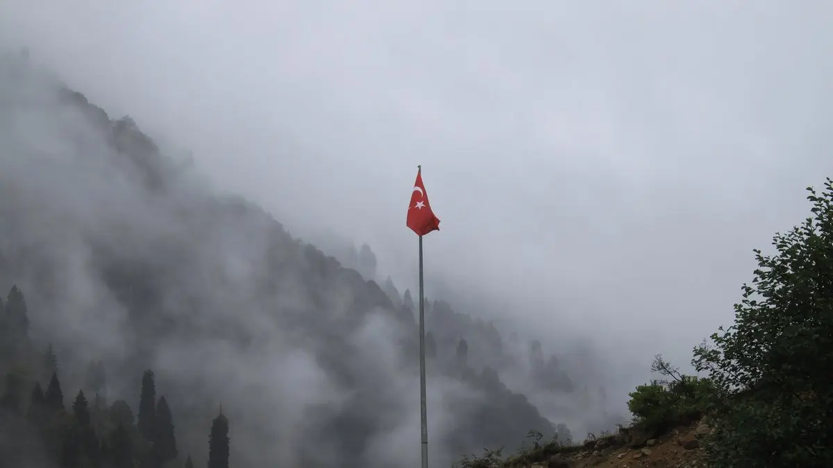 Sisli yeşil dağların önünde yüksek bir direkte tek başına dalgalanan Türk bayrağı, Çamlıhemşin