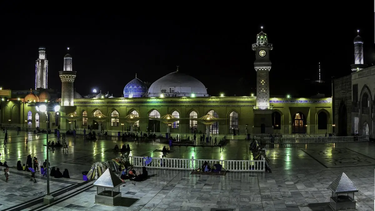 Bağdat'taki Abdülkadir Geylani Türbesi ve Camii'nin gece ışıklandırılmış avlusu, yeşil ve mavi kubbeleri ve minareleri