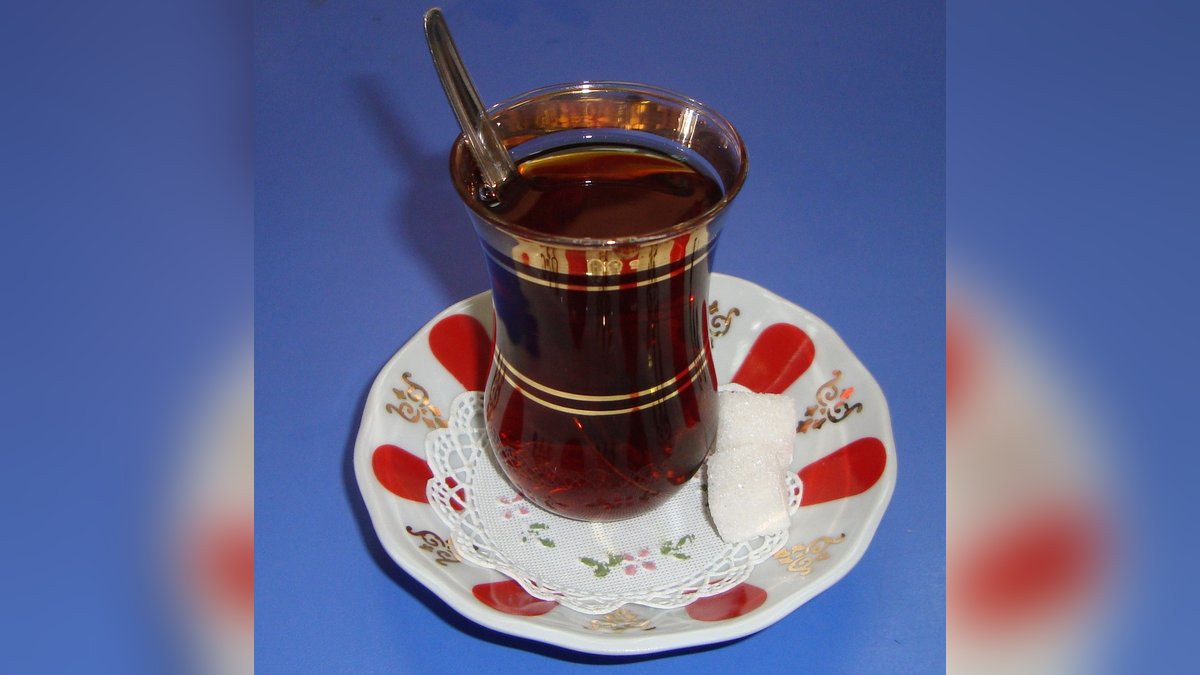 Kırmızı desenli porselen tabağın üzerinde ince belli bardakta demli Türk çayı ve iki kesme şeker