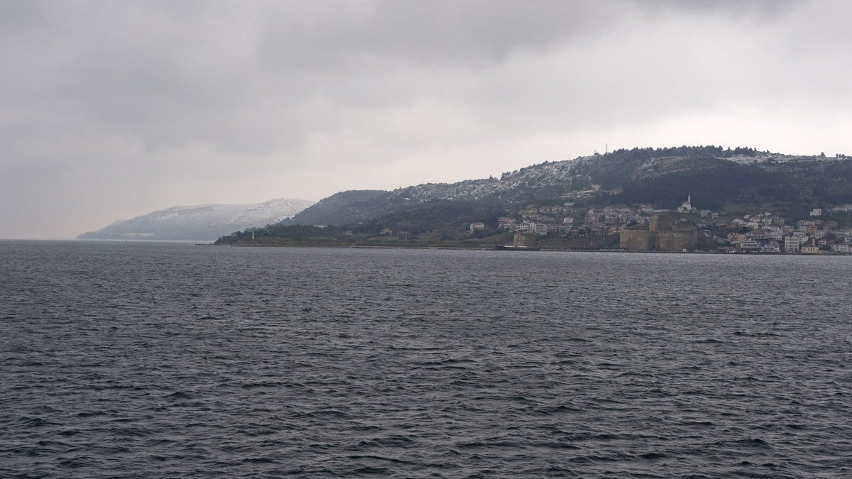 Bulutlu bir günde Çanakkale Boğazı'nın gri suları ve karşı kıyıda tepelere yayılmış yerleşim