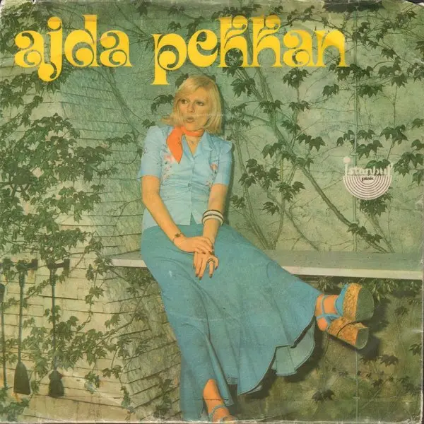 Ajda Pekkan’ın Diva albüm kapağı; turuncu tonlarda, kızıl saçlı Ajda Pekkan’ın omzunun üzerinden bakan yakın çekim fotoğrafı ve sarı Diva yazısı
