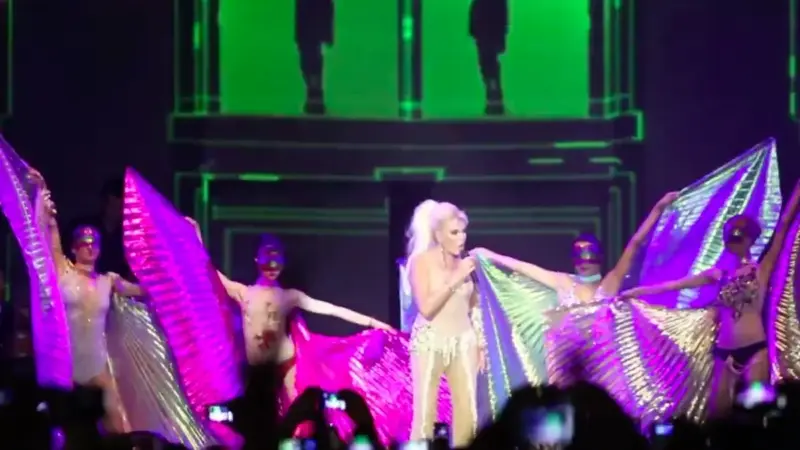 Ajda Pekkan’ın 2012’deki Kuruçeşme Arena konserinde, açık renkli parlak kostümüyle elinde mikrofon şarkı söylerken; iki yanında altın ve mor renkli kanat pelerinler açmış maskeli dansçılar