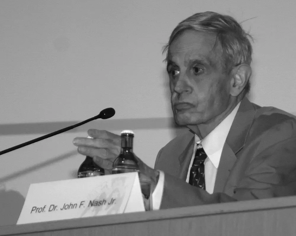 Gerçek John Forbes Nash Jr. 2006’da Köln’de bir oyun kuramı sempozyumunda kürsüde, önünde Prof. Dr. John F. Nash Jr. yazan isimlik