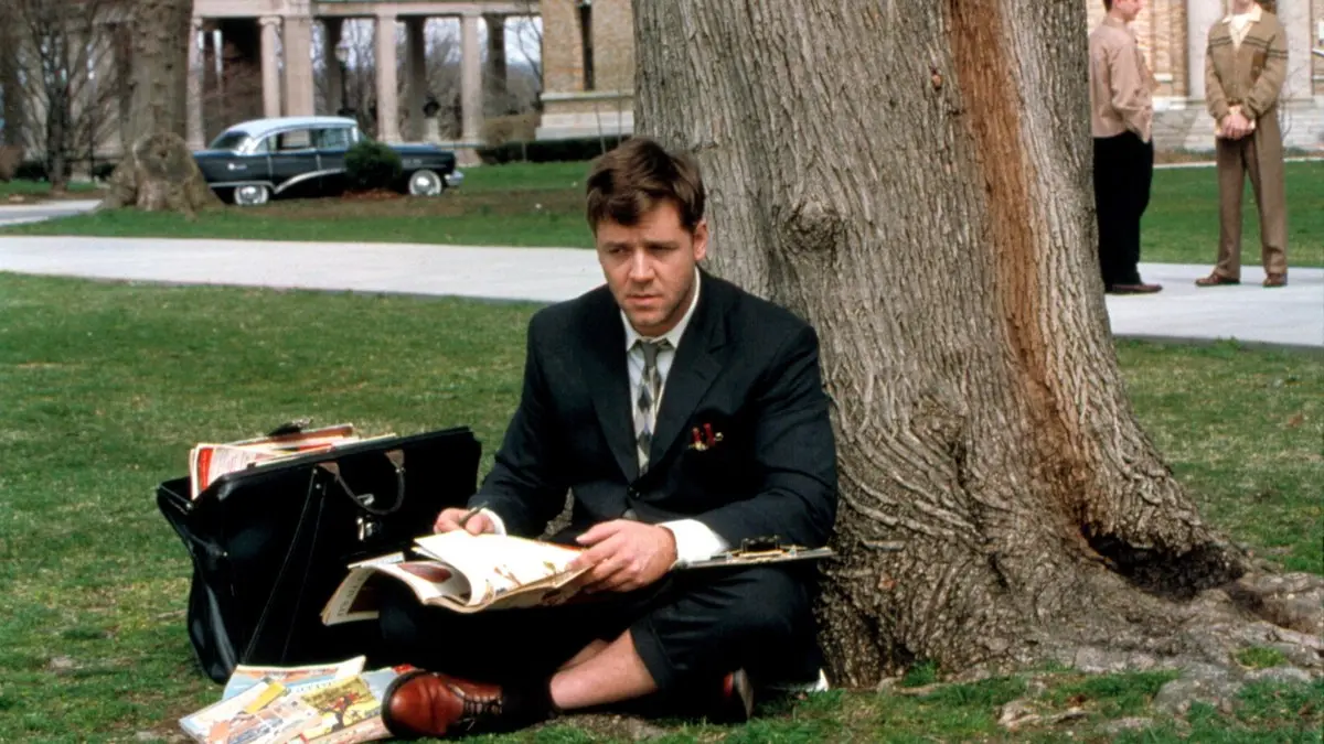 Akıl Oyunları filminden sahne: Princeton kampüsünde ağacın dibindeki çimenlere oturmuş, kucağındaki kâğıtlara bakan takım elbiseli genç John Nash