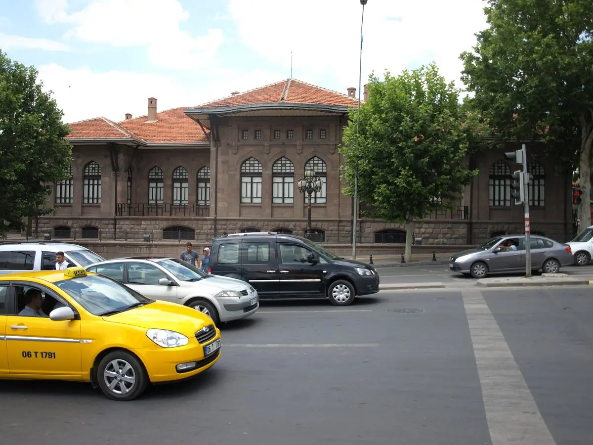 Ulus’taki Kurtuluş Savaşı Müzesi’nin kırmızı kiremit çatılı taş binası; önünde ağaçlar, caddede sarı bir taksi ve otomobiller