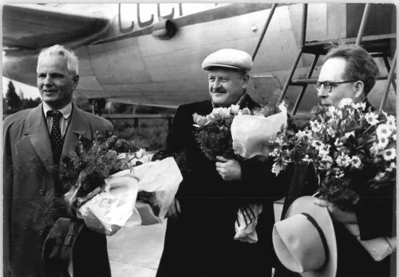 Kasketli Nâzım Hikmet'in elinde çiçek demetiyle, iki Sovyet yazarın arasında bir uçağın önünde gülümsediği siyah-beyaz fotoğraf