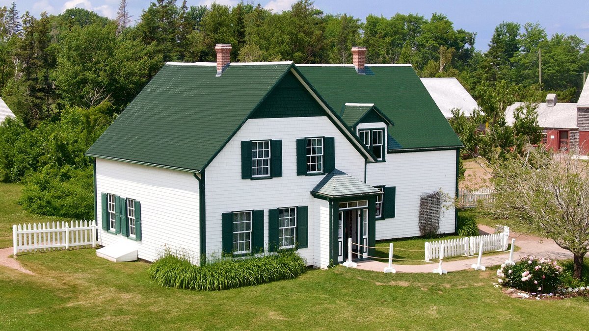 Yeşil panjurlu, koyu yeşil çatılı beyaz ahşap Green Gables evi, önünde biçilmiş çimenlik ve beyaz çit