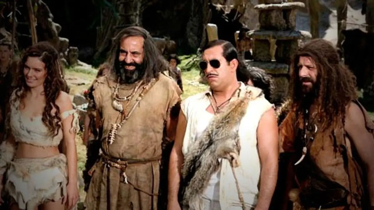 A.R.O.G filminden tanıtım karesi: taş devri köyünde güneş gözlüklü, bıyıklı ve omzunda hayvan postu olan Arif; yanında uzun saçlı, sakallı iki köylü ve hayvan postundan kıyafetli genç bir kadın