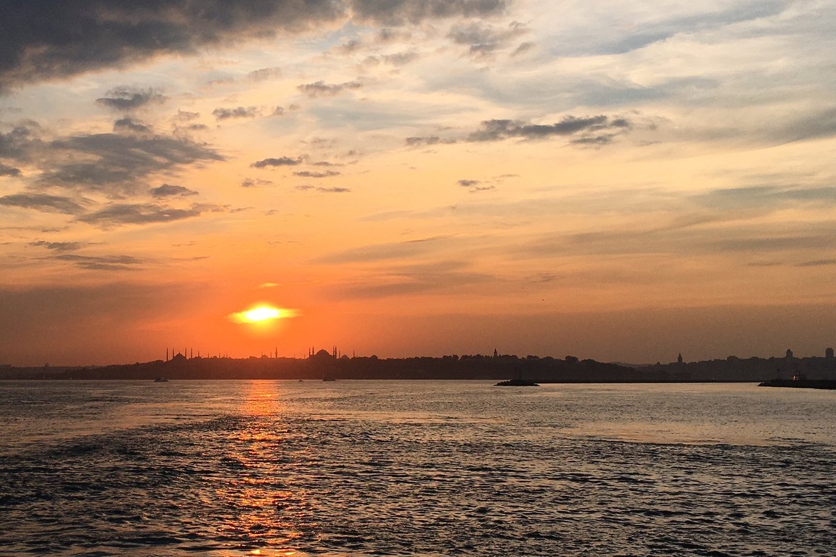 İstanbul Boğazı'nda bulutlu gökyüzünde turuncu renklerle batan güneş ve suya düşen ışığı