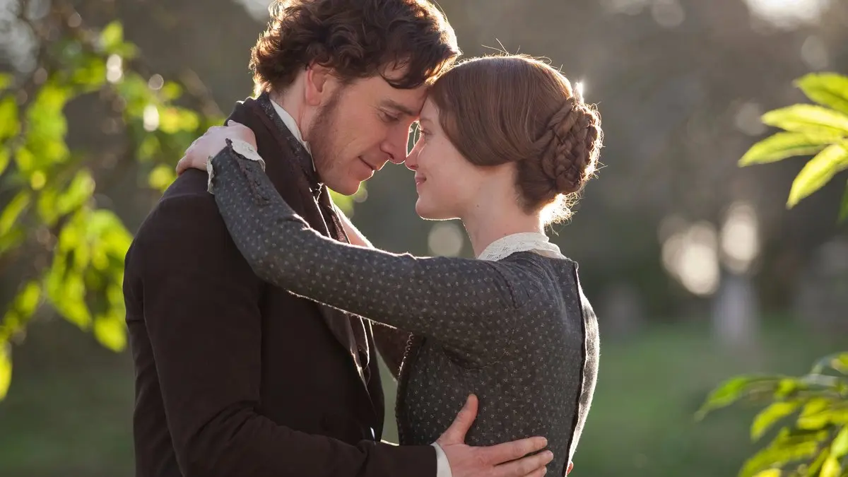 Jane Eyre (2011) filminden sahne: yeşil bir bahçede alınlarını birbirine dayamış Bay Rochester rolündeki Michael Fassbender ve Jane rolündeki Mia Wasikowska
