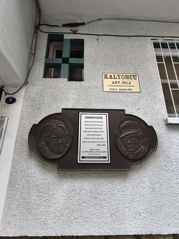 Karşıyaka’da Kalyoncu Apartmanı duvarındaki plaket; Biket İlhan ve Attilâ İlhan kabartmaları arasında Yağmur Kaçağı şiirinden dizeler