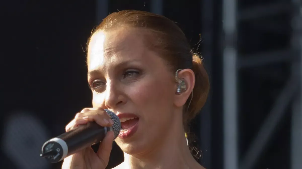 Sertab Erener'in saçlarını arkada toplamış hâlde, kulağında sahne kulaklığıyla mikrofona şarkı söylerken çekilmiş yakın plan konser fotoğrafı