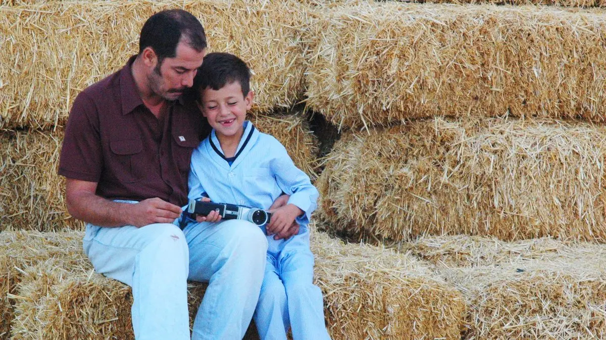 Babam ve Oğlum filminden sahne: saman balyalarının arasında oturan Sadık ve Deniz, Sadık’ın elindeki dergiye birlikte bakıyor