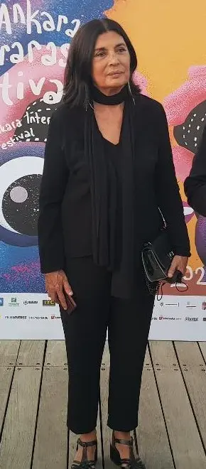 Siyah kıyafetli oyuncu Şerif Sezer, renkli 31. Ankara Uluslararası Film Festivali panosunun önünde ayakta duruyor