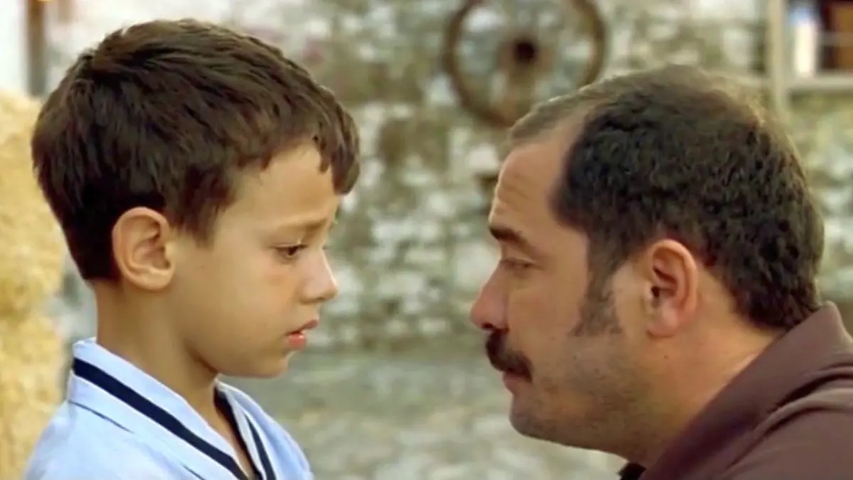 Babam ve Oğlum filminden yakın plan: beyaz yakalı küçük Deniz ile babası Sadık yüz yüze bakışıyor