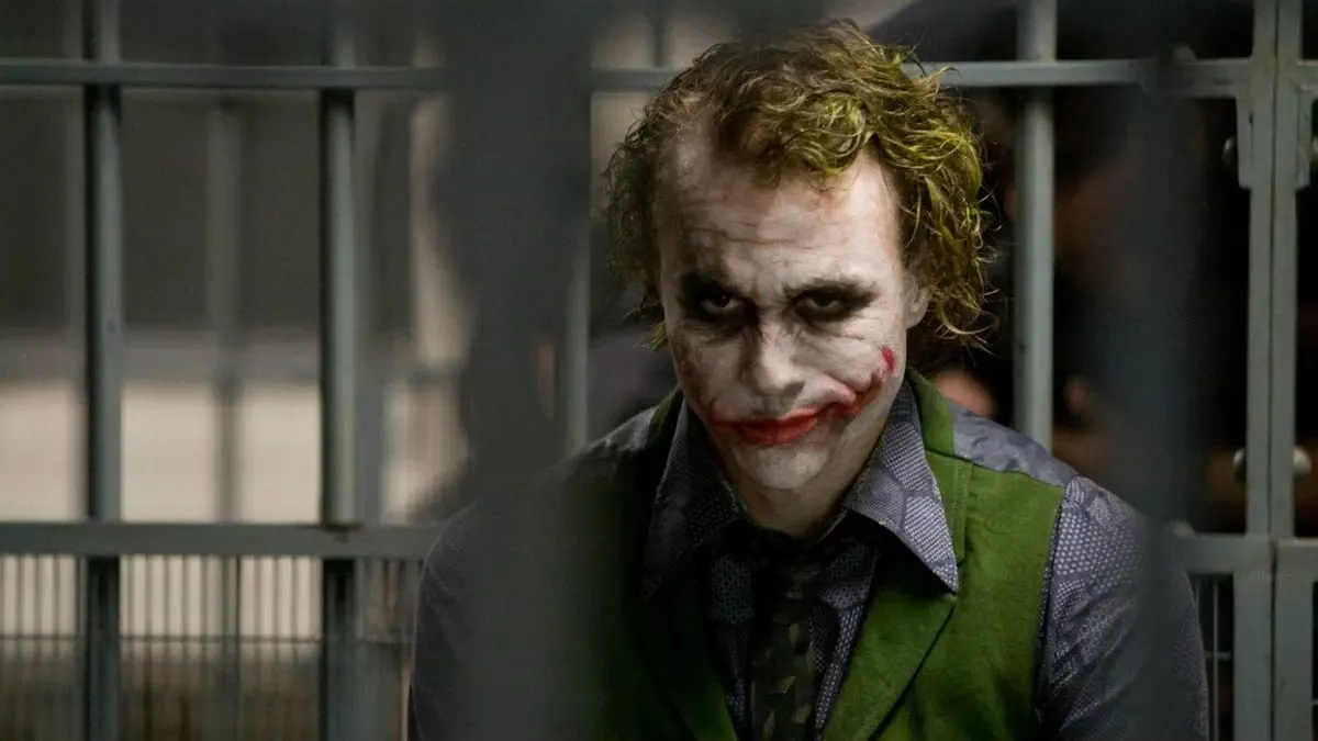 Kara Şövalye filminden sahne: parmaklıkların önünde, dağınık yeşil saçları ve bulaşmış makyajıyla Joker rolündeki Heath Ledger