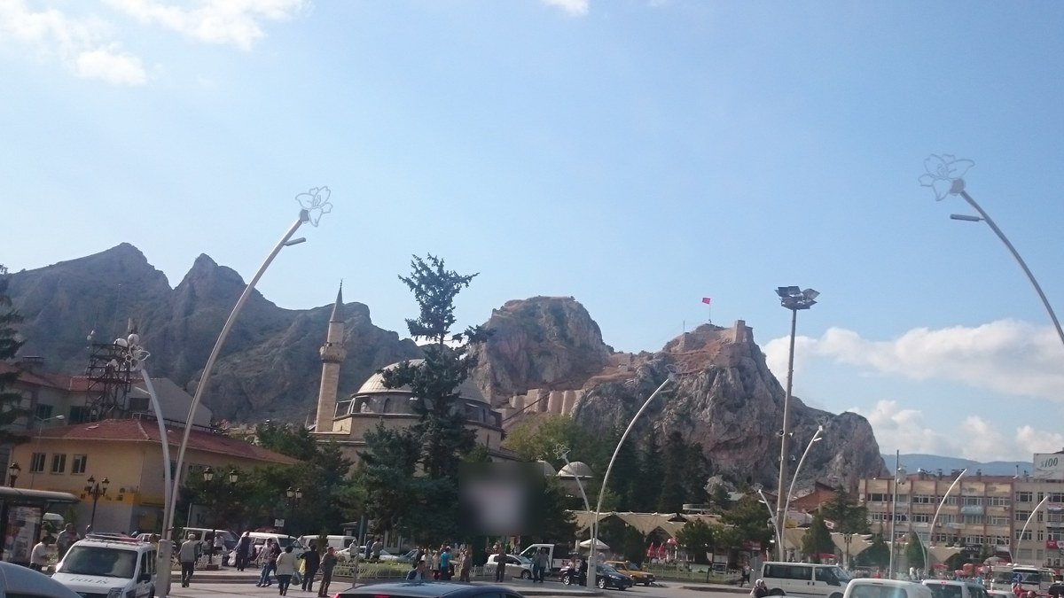 Tokat şehir meydanından görünen kayalık dağlar, tepedeki Tokat Kalesi ve minareli bir cami