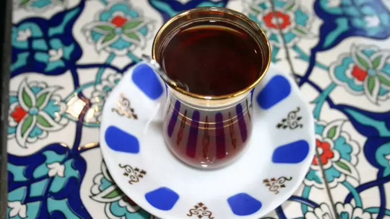 Çini desenli masa üzerinde mavi benekli tabağında, ağzına kadar dolu ince belli bardakta demli Türk çayı