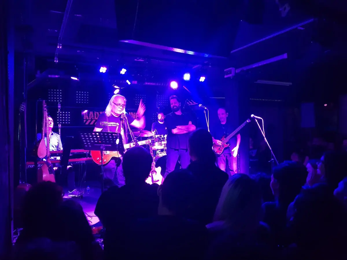 Moğollar grubu sahnede; mor ve mavi ışıklar altında elektro gitar çalan beyaz saçlı Cahit Berkay ve arkasında grup üyeleri