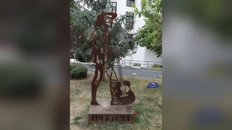 Kadıköy Moda’da çimenlerin üzerinde duran, şapkalı ve gitarına yaslanmış Cem Karaca silüetini gösteren paslı metal heykel; kaidesinde Cem Karaca yazıyor
