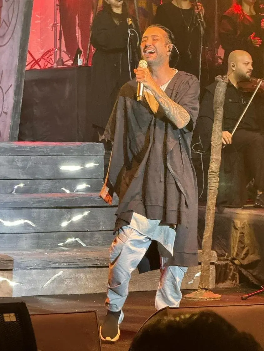 Tan Taşçı’nın 2024’teki bir konserinde gri uzun ceket ve yırtık kot pantolonla sahnede mikrofonla şarkı söylediği an