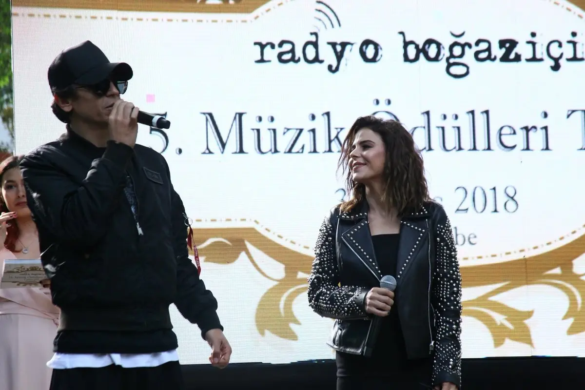 Ersay Üner’in şapkası ve siyah kıyafetiyle Simge’nin yanında 2018’deki 15. Radyo Boğaziçi Müzik Ödülleri sahnesinde mikrofonla konuştuğu an
