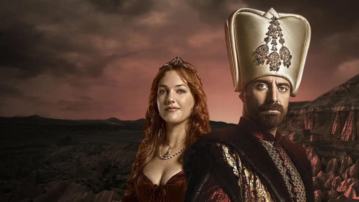 Muhteşem Yüzyıl dizisinin tanıtım görselinde bulutlu gökyüzü altında yüksek kavuklu Kanuni Sultan Süleyman rolündeki Halit Ergenç ve kızıl saçlı Hürrem rolündeki Meryem Uzerli