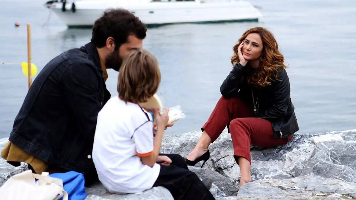 Poyraz Karayel dizisinden deniz kıyısındaki kayalıklarda oturan Poyraz, yanındaki çocuk ve kırmızı pantolonlu Ayşegül