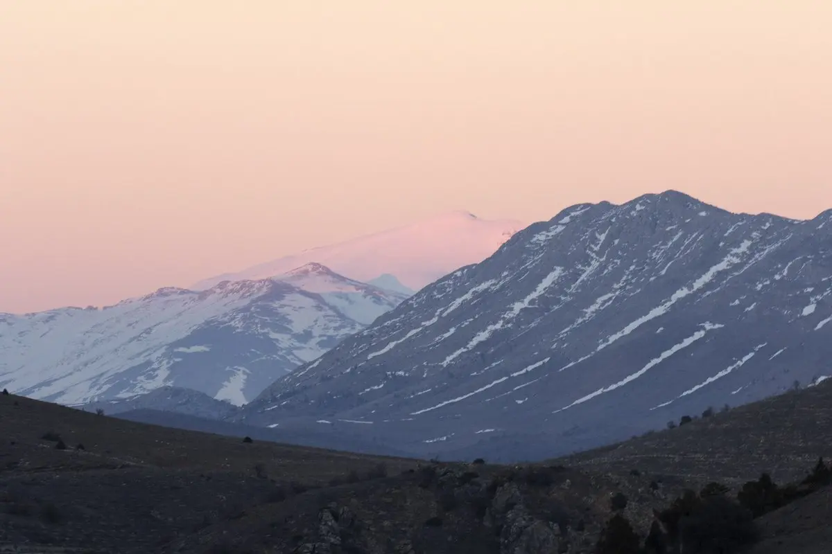 Gün batımında karla kaplı Binboğa Dağları’nın zirveleri, önde kararmış tepeler ve pembe tonlu gökyüzü