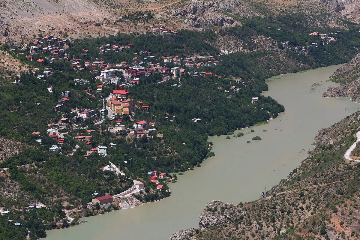 Kemaliye (Eğin) ilçesinin yüksekten görünümü: Fırat Nehri’nin kıyısında yeşil ağaçlar arasına serpilmiş evler ve çevresindeki çıplak dağ yamaçları