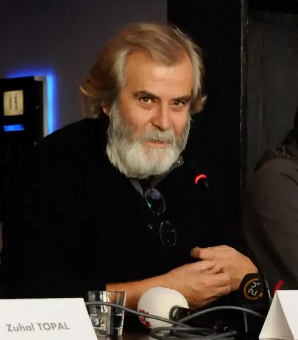 Tarık Akan’ın 2008’de bir basın toplantısında çekilmiş portresi: kırlaşmış saçları ve sakalıyla mikrofonun önünde oturuyor