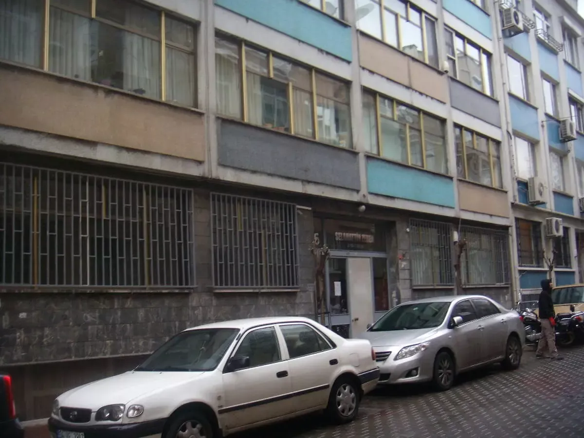 Kapıcılar Kralı filminin çekildiği, cephesi açık mavi ve krem renkli çok katlı İstanbul apartmanı; önünde park etmiş otomobiller