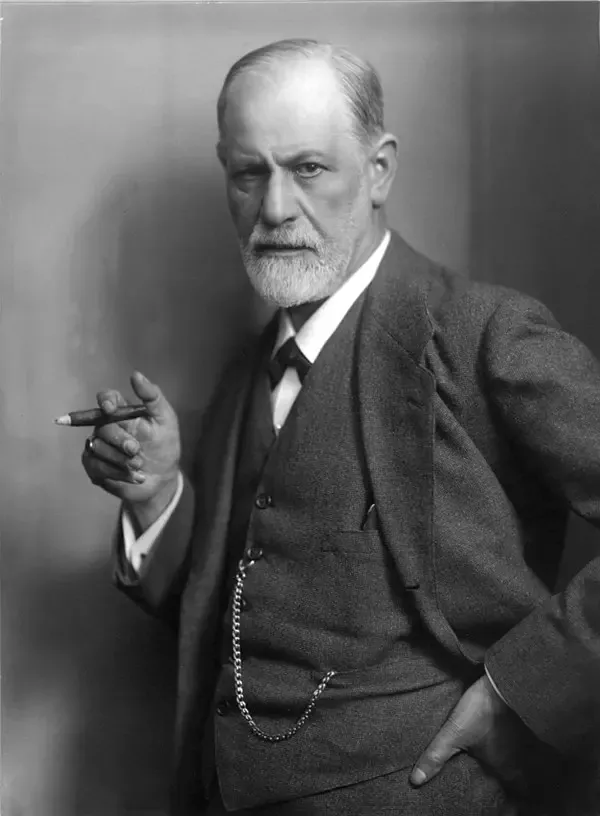 Sigmund Freud’un siyah beyaz portresi; takım elbiseli, beyaz sakallı Freud elinde bir puro tutarak doğrudan objektife bakıyor