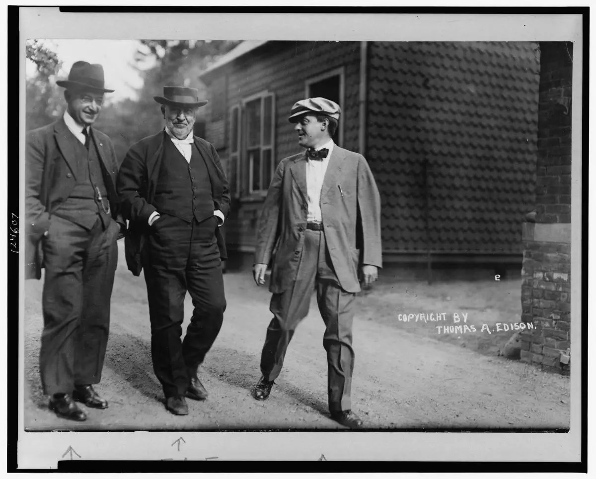 Thomas Edison, laboratuvarının avlusunda takım elbiseli iki çalışma arkadaşıyla yürürken çekilmiş siyah beyaz fotoğraf