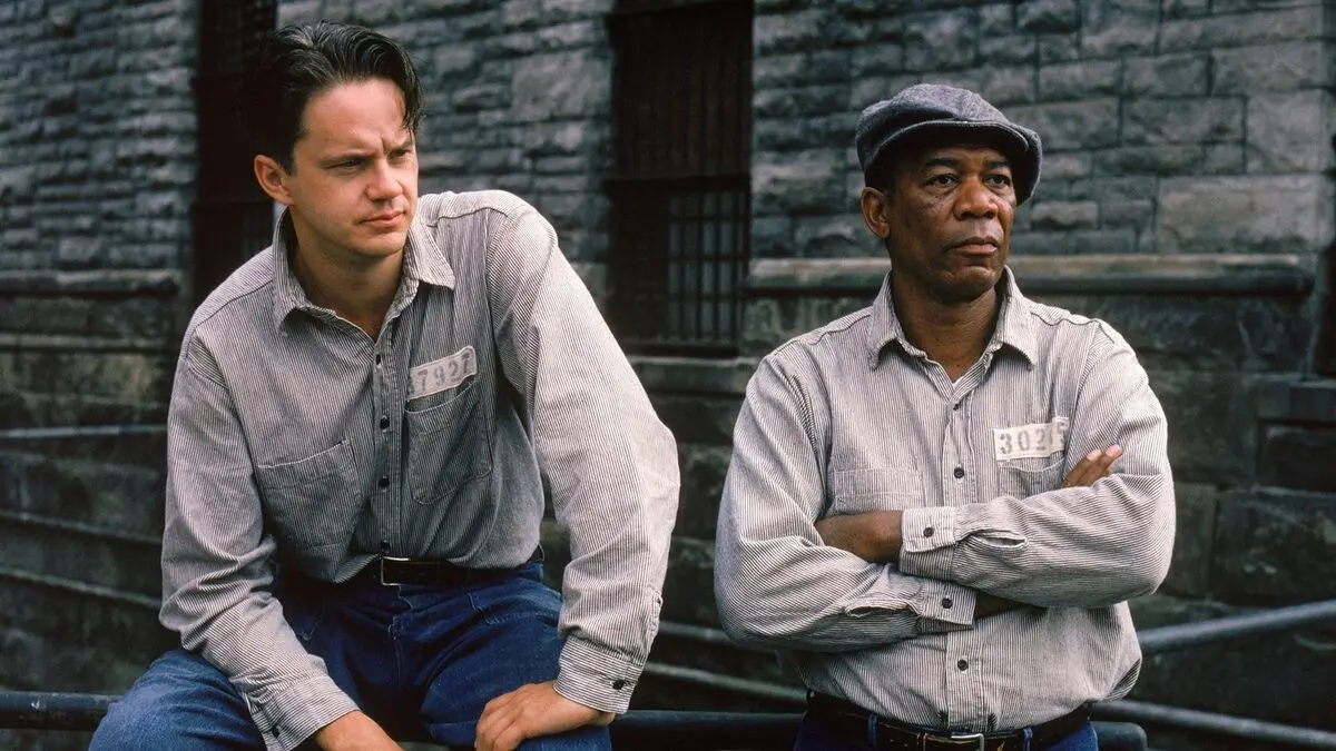 Esaretin Bedeli filminde taş duvarlı hapishane bahçesinde basamaklara oturmuş, gri mahkûm gömlekli Andy Dufresne (Tim Robbins) ve kollarını kavuşturmuş, şapkalı Red (Morgan Freeman)