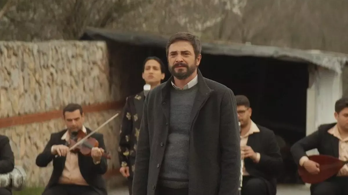 Taş duvarlı bir avluda, ortada koyu renk paltolu Baki (Ahmet Kural) dururken çevresinde keman, bağlama ve darbuka çalan takım elbiseli müzisyenler