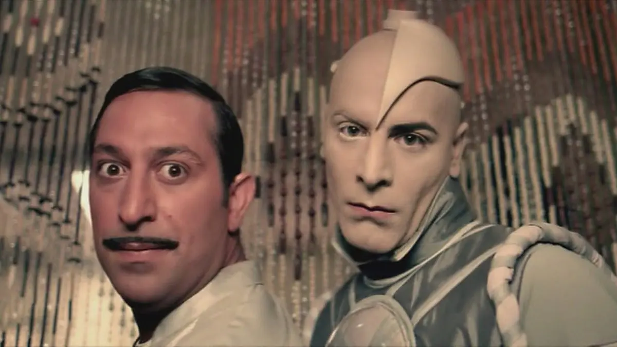 G.O.R.A. filminden tanıtım karesi: ince bıyıklı Arif ile gümüş renkli Robot 216 yan yana, şaşkın bakışlarla öne bakıyor