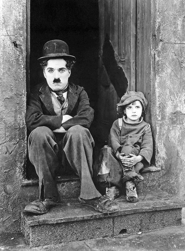 Charlie Chaplin ve küçük Jackie Coogan, Yumurcak filminin tanıtım fotoğrafında yıkık bir kapı eşiğinde yan yana oturuyor