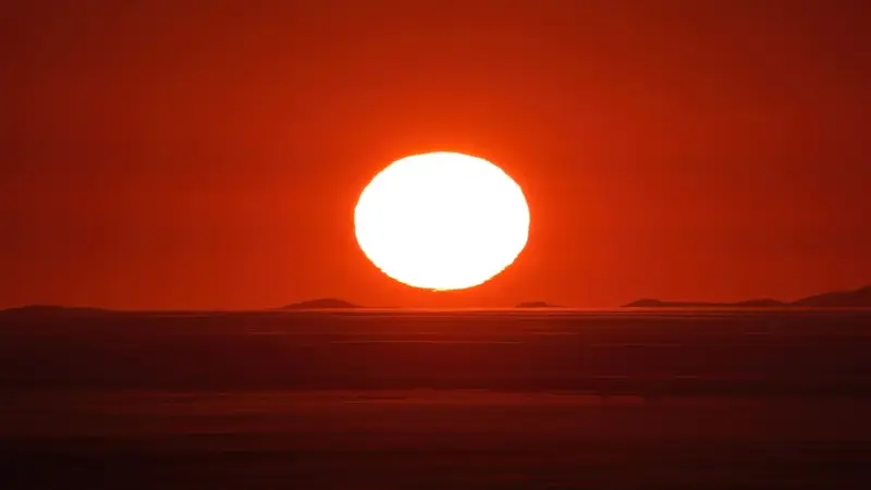 Namib Çölü’nde ufka yaklaşan kocaman, parlak beyaz güneş diski; gökyüzü ve çöl koyu kırmızı ve turuncu tonlarda