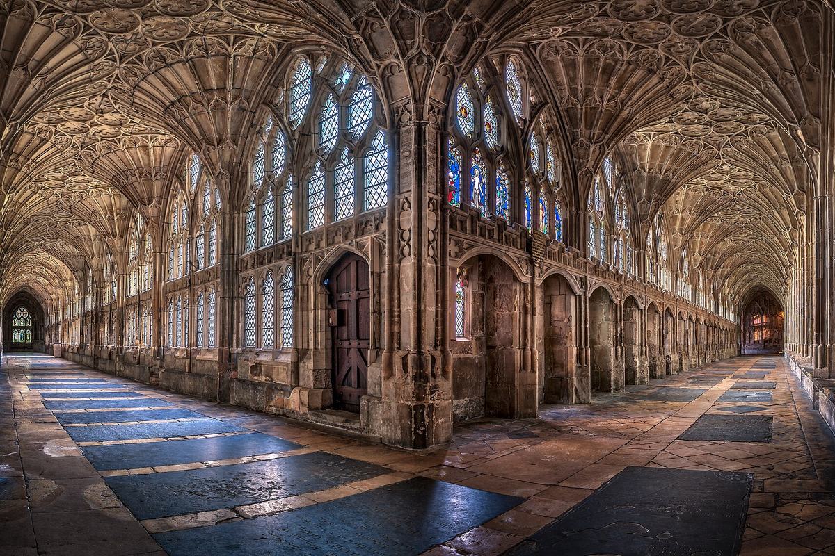 Gloucester Katedrali'nin taş zeminli manastır avlusu koridorunda yelpaze tonozlu tavan ve renkli vitraylı pencereler